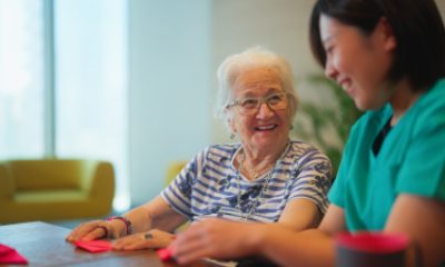 Older woman smiles at a young health caregiver as they fold paper at a table