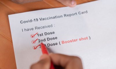 COVID-19 vaccination card in hands showing booster shot box checked