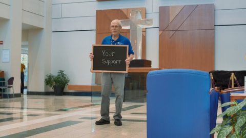 Phil Cahoon holding a blackboard with the words "Your Support" written out