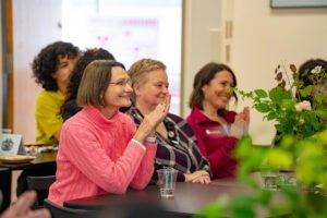 Photo of three women sitting at a table and clapping