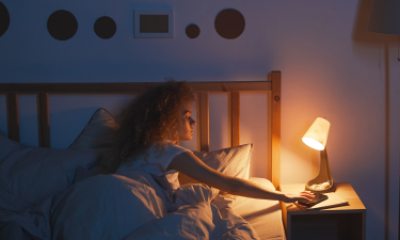 Woman in bed reaches out to cell phone on nightstand