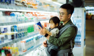Father holds young daughter as he reads ingredient list on bottle in grocery store