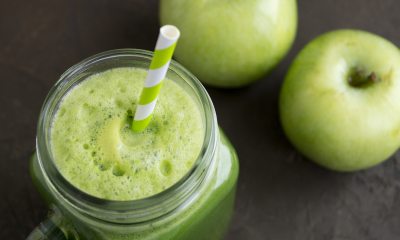 A green smoothie with a straw in a mason jar and green apples in the background