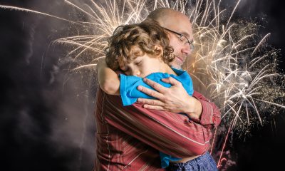Father hugs young son while a fireworks display goes on in the background