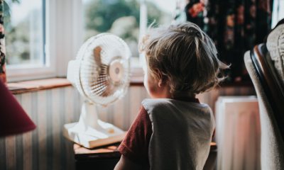 Young child stands in front of a cooling fan indoors