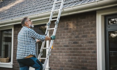 Man climbing up a ladder to clean the gutters on his house.