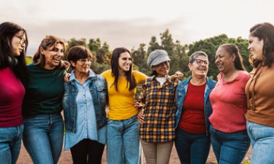 A group of 8 smiling women of various ages in an outdoor setting