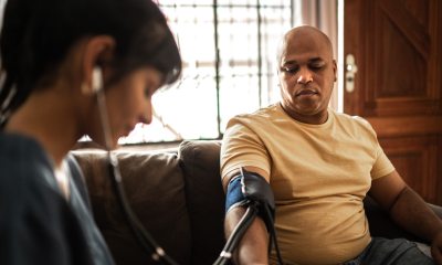 Young healthcare provider takes blood pressure reading for a Black man sitting on a couch