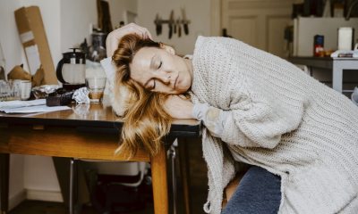 Sleepy woman with long blond hair slumps over a kitchen table