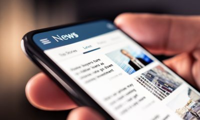 Closeup of hand holding a cell phone with news on the screen