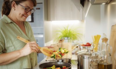 Smiling older woman stirs veggies in a pan on the stove