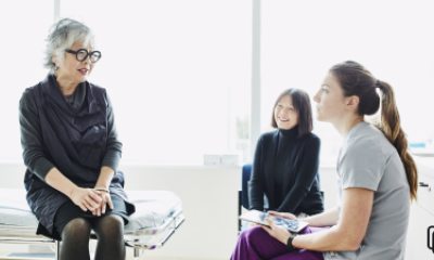 gray-haired woman on an exam table talks with a healthcare provider and dark-haired woman