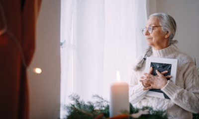 Woman with long silver hair holds a book to her chest and looks out the window