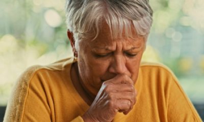 Woman with short silver hair coughs into her hand