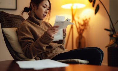 Asian women in brown sweater sitting in bedroom reviewing receipts