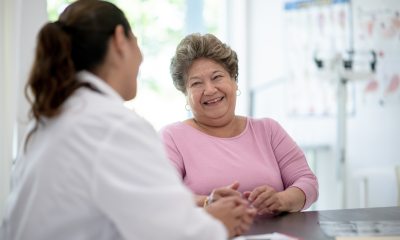 Smiling woman with short salt-&-pepper hair sits and talks with a doctor in a white coat