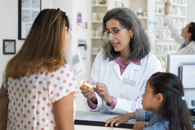 Female pharmacist talking with mother and child while holding a prescription bottle