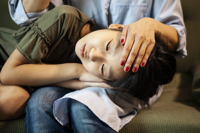Close up of face of an Asian girl resting her head in the lap of a woman