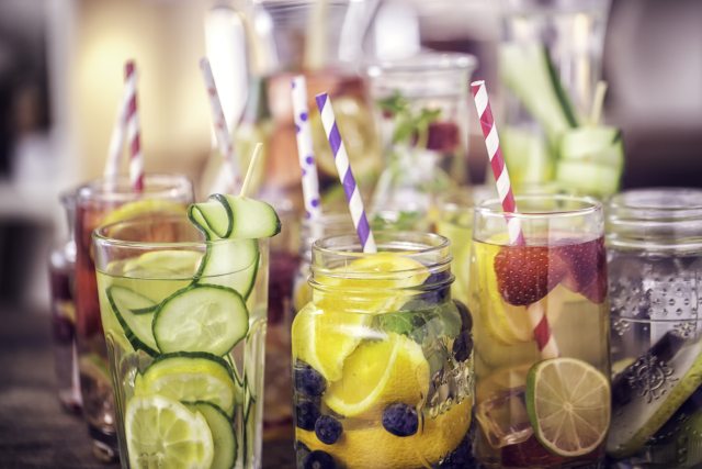 Image of water glasses with colorful striped straws and infused with cucumber, fruit and mint