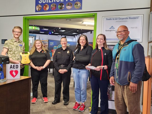 Eugene Science Center staff and others stand in the center's building to receive the donation of an automatic external defibrillator.