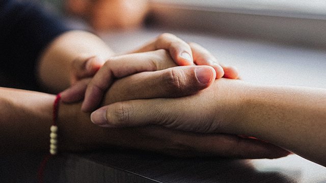 A person holds the hand of another person in a gesture of comfort