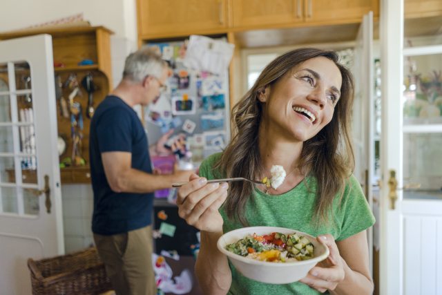 Middle aged woman happily eats a bowl of vegetables