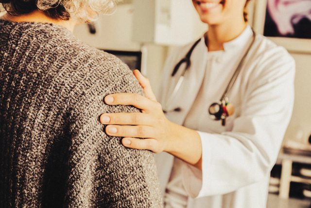 A smiling healthcare provider placing a hand on a patient's shoulder as a gesture of comfort