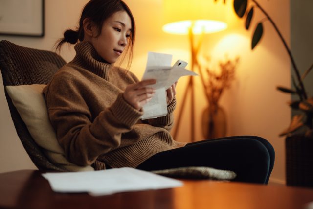 Asian women in brown sweater sitting in bedroom reviewing receipts