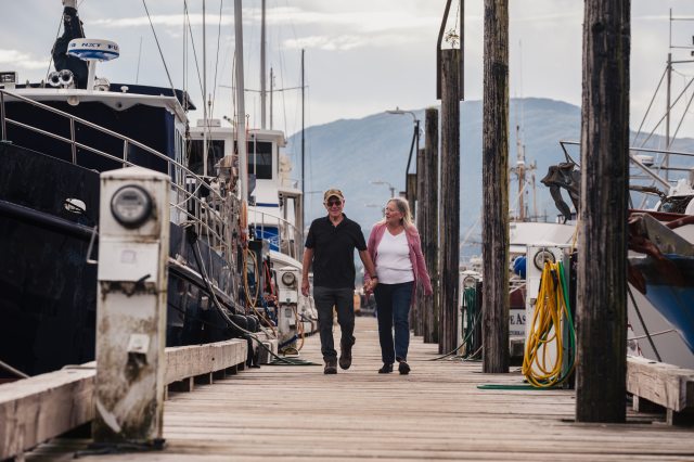 Photo of an older couple holding hands and walking down a dock toward the camera