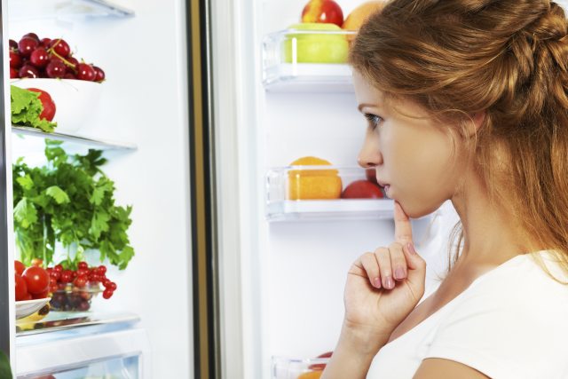 A woman looks into her refrigerator and contemplates what she should eat